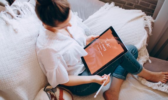 A woman relaxes on a sofa with a digital tablet, enjoying leisure time in a cozy home environment.